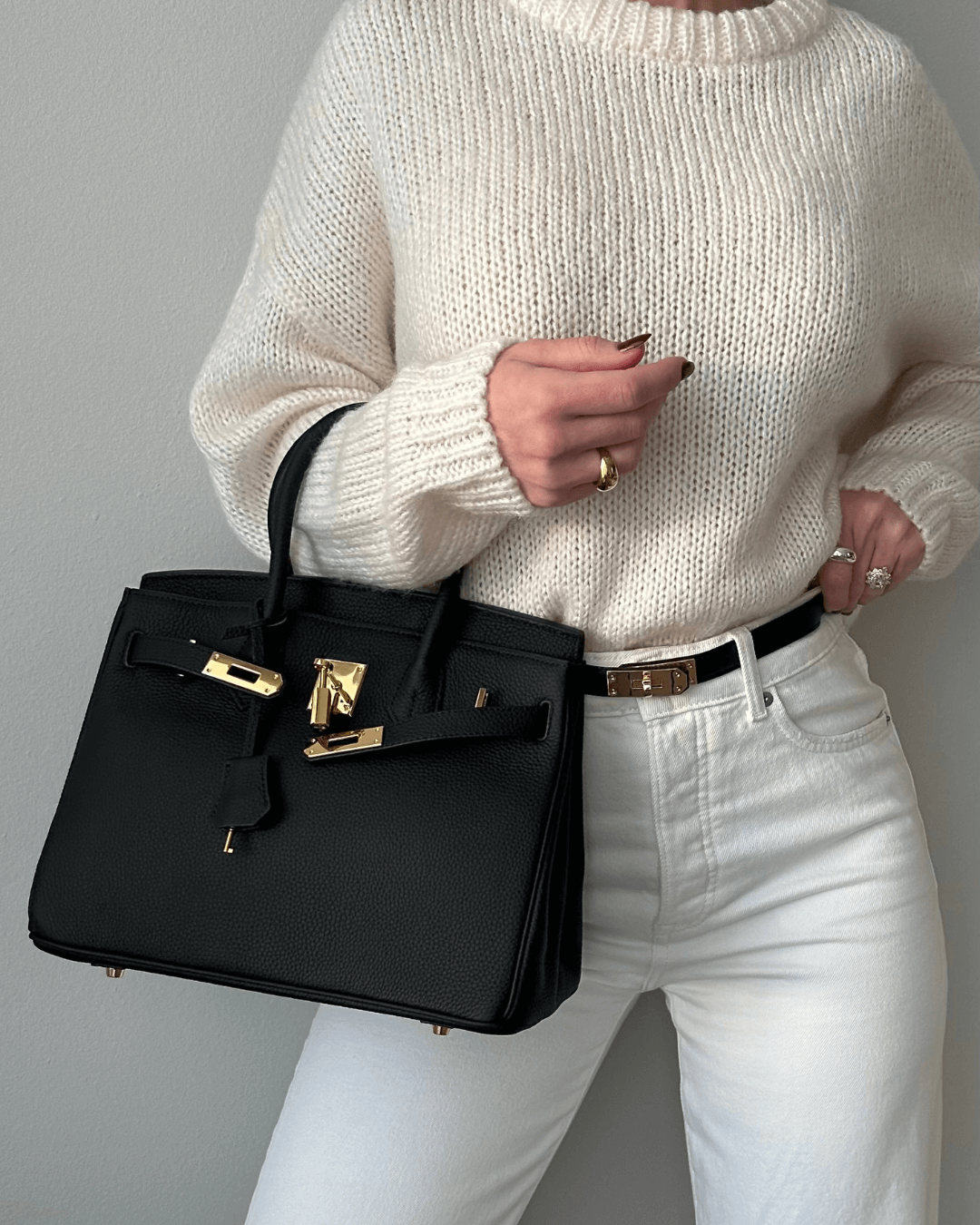 Image showing a woman holding an elegant handbag with a sleek design, featuring gold hardware and a structured shape, paired with casual attire for a stylish, sophisticated look.
