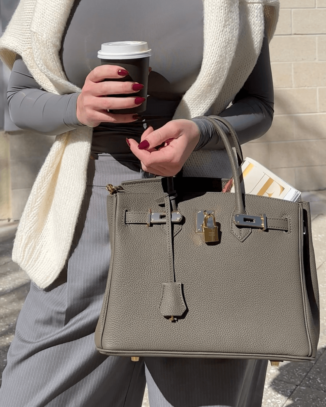 Image showing a woman holding an elegant handbag with a sleek design, featuring gold hardware and a structured shape, paired with casual attire for a stylish, sophisticated look.