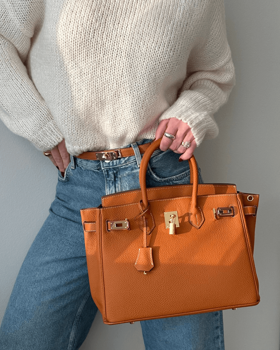 Image showing a woman holding an elegant handbag with a sleek design, featuring gold hardware and a structured shape, paired with casual attire for a stylish, sophisticated look.